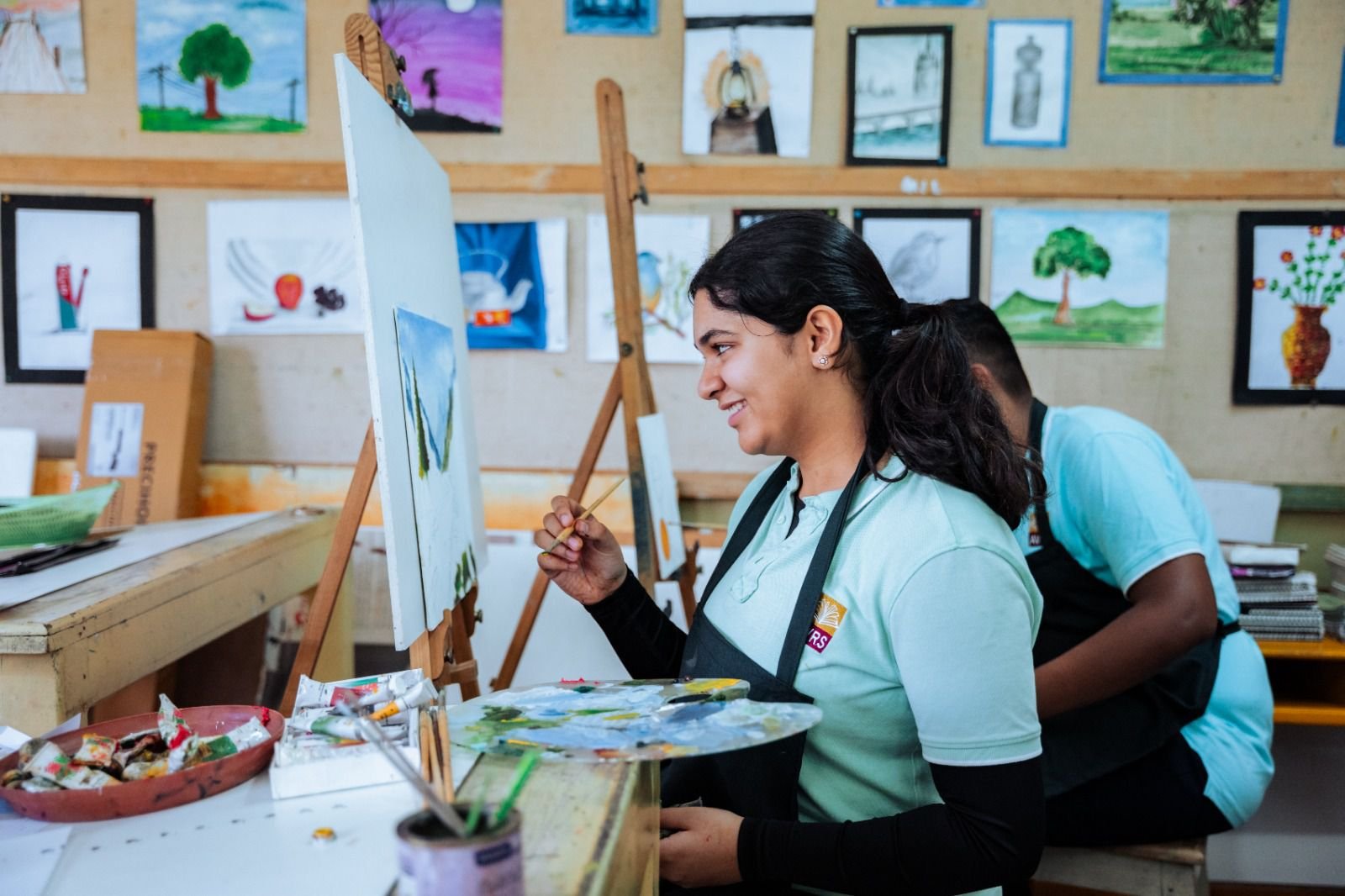 A student painting a landscape on canvas in the art studio